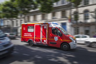 Blurred French emergency vehicle rushing through city street with blue lights flashing