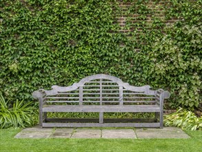 Wooden bench designed by Sir Edwin Lutyens in the rose garden at Sissinghurst Castle with Clematis 'Perle d'Azur' at back