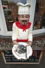 Figure of a chef holding a plate with a fish dish outside a restaurant