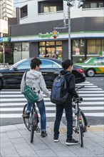 Two teenagers with bicycles waiting at a traffic light with zebra crossing