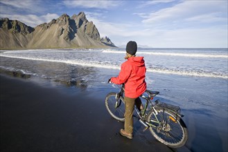 Woman riding a bicycle on the beach in front of Mt Vestrahorn near Hoefn
