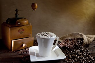 Cup of cappuccino with coffee beans and an old coffee grinder