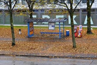 A bus stop surrounded by autumn foliage in the rain