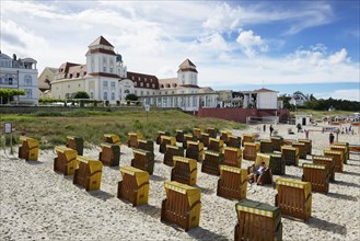 Roofed wicker beach chairs on the beach in front of the Kurhaus spa building