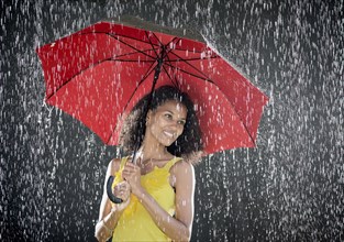 Young Cuban woman holding a red umbrella while enjoying the rain