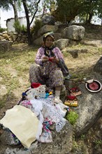 An old woman with reading glasses is selling lace to tourists