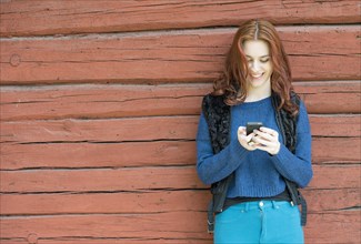 Young woman with red hair smiling and looking at her mobile phone