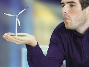 Man blowing a miniature wind turbine in his hand