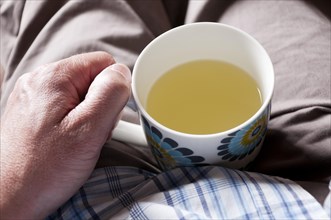 Man suffering from a cold holding a mug of lemsip in his lap
