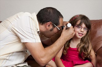 Doctor on a home visit examining a girl with an otoscope