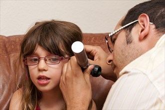 Doctor during a home visit examining a girl with an otoscope