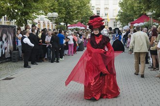 Woman in a red and black costume with a mask taking part in the artist's procession