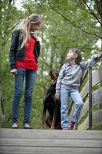 Two girls standing with a Doberman on a bridge