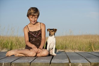 Girl sitting with a Dansk-Svensk Gardshund or Danish-Swedish Farmdog on a jetty