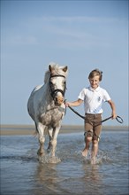 Girl leading a pony through the water