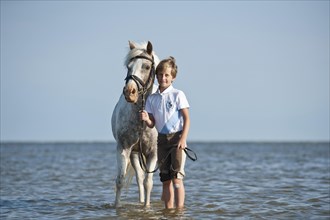 Girl leading a pony through the water