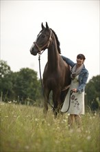 Woman standing beside a Hanoverian horse in a meadow