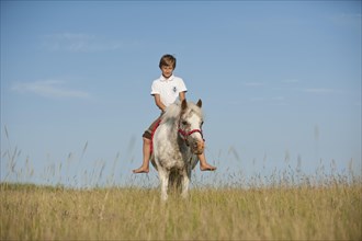 Girl riding a pony across a meadow
