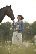 Woman standing beside a Hanoverian horse in a meadow