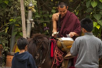 Buddhist monk on horseback with a begging bowl collecting alms in the morning