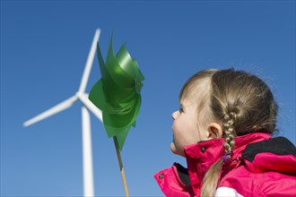 Girl holding a small pinwheel in front of a large wind turbine
