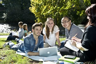 Students with a laptop and books on a meadow