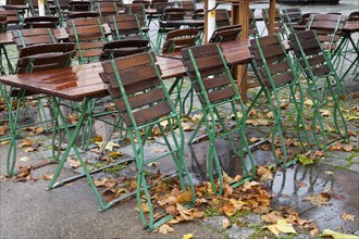 Empty tables and chairs of an outdoor restaurant in the rain with autumn leaves in the historic city centre of Cologne