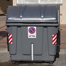 Wheeled trash can with a No parking sign standing on the roadside