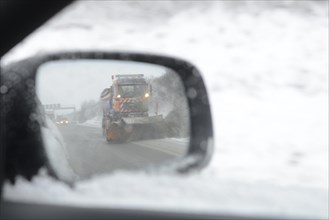 Car mirror reflecting a snow-clearing vehicle from the motorway maintenance authorities in operation on the A8 motorway