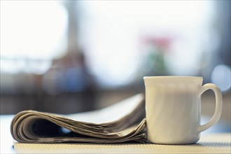 A cup of coffee and a newspaper lying on a kitchen table