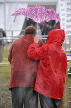 Couple sheltering under small umbrella during thunderstorm at agricultural show