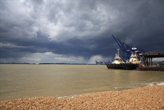 Tugboats moored at harbour of container port with passing rainclouds