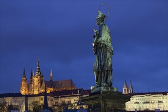 Statue of Nepomuk with castle and cathedral illuminated at night