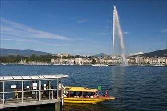 Ferry boat at the dock of the Geneva ferry company Mouettes genevoises in front of the giant fountain Jet d'Eau