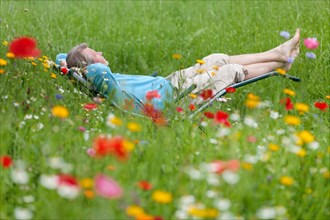 Man relaxing while lying in a deck chair in a flower meadow