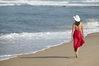 Rear view of a young woman wearing a bikini and a red sarong walking along a beach in summer