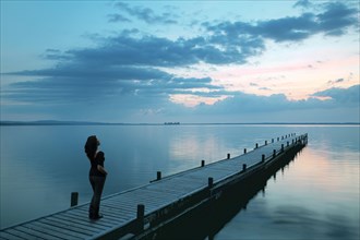 Young woman standing on boat dock on the lake admiring the evening sky in the blue hour