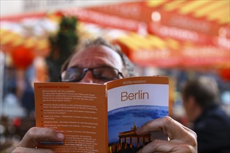 Man concentrating while reading a Berlin guide while sitting at a sidewalk cafe