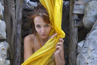 Young woman with a yellow silk scarf in front of a stone hut