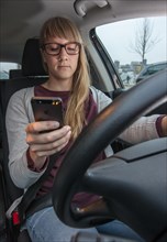 Young woman driving a car while texting on her cell phone