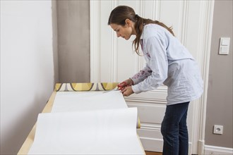 Young woman preparing wallpaper for wallpapering the walls