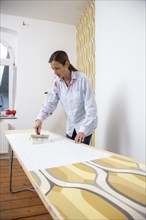 Young woman preparing wallpaper for wallpapering a wall