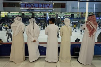 Arabs wearing traditional white dishdasha robes watching ice skaters