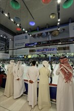 Arabs wearing traditional white dishdasha robes watching ice skaters