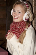 Smiling young woman wearing ear warmers and a scarf in a hiking hut