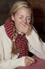 Young woman wearing a scarf sitting at the table of a hiking hut and yawning