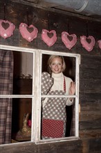 Smiling young woman wearing an apron standing at the window of a hiking hut
