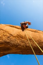 Young man abseiling from a rock arch