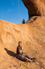 Young man abseiling from a rock arch