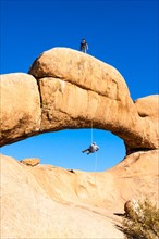 Two men abseiling from a rock arch